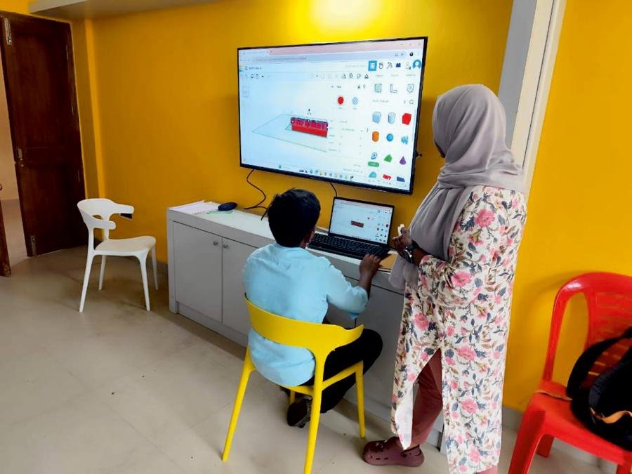 Student designing a 3D model on a large screen with a mentor